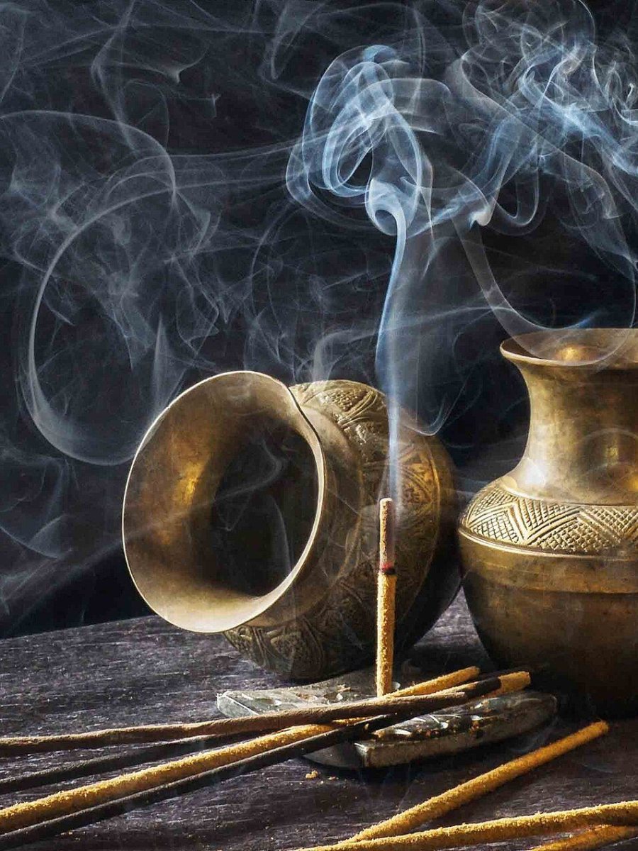 أوانٍ نحاسية يتصاعد منها دخان البخور على خلفية داكنة